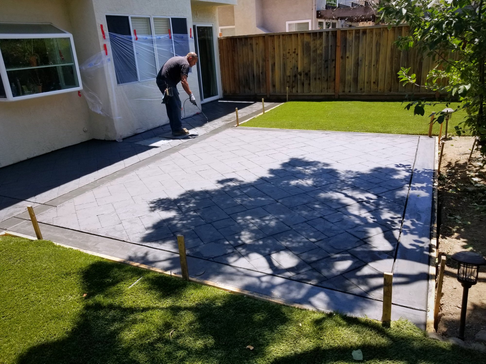 Crew sealing a freshly stamped two-tone concrete patio